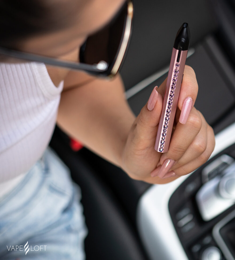 A woman holding a Swarovski Caliburn Pod Vape while in the car