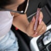 A woman holding a Swarovski Caliburn Pod Vape while in the car