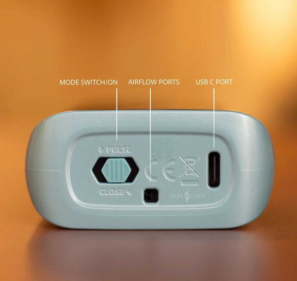 Close-up of a vape device showing mode switch, airflow ports, and USB-C port on a wooden surface.